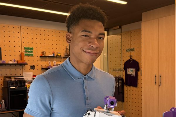 A young man smiling holds a robot made as part of a school project.