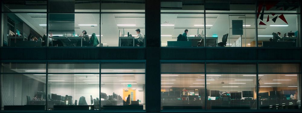 Office building windows at night with workers inside.